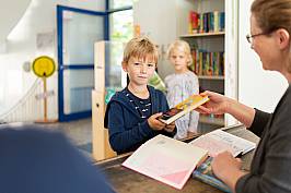 Junge bekommt von einer Lehrerin ein Buch überreicht