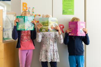 Drei Kinder verstecke sich hinter ihren Büchern