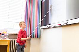 Schüler zeigt mit einem Zeigestock auf ein Whiteboard