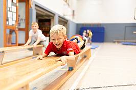 Schüler zieht sich mit seinen Armen über eine Bank in der Sporthalle