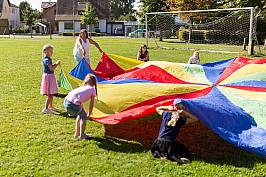 Kinder spielen auf einer Wiese mit einem großen bunten Tuch