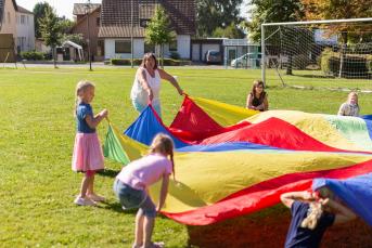 Kinder spielen auf einer Wiese mit einem großen bunten Tuch