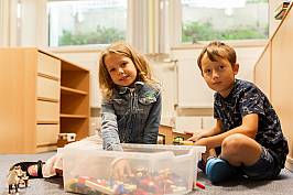 Zwei Schüler sitzen auf dem Boden uns suchen Legosteine aus einer großen Kiste